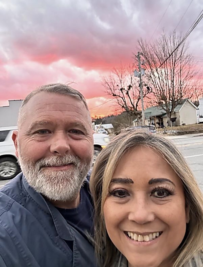 Ryan and Laura smiling together beneath a pink sunset sky
